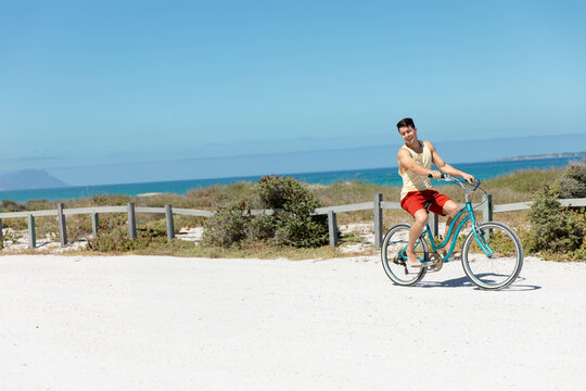 Fototapeta Cyclist is riding teal cruiser bicycle along sandy path near turquoise ocean, fence lining route