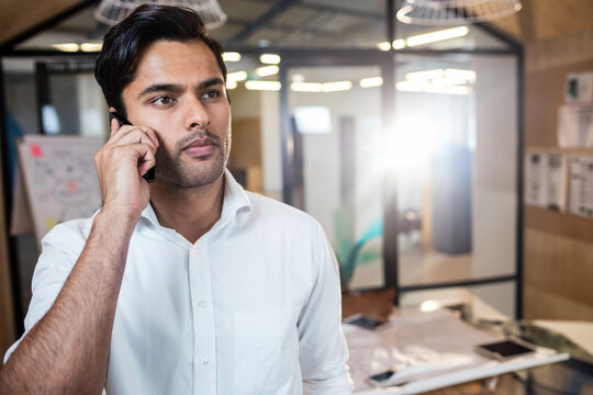 Asian man standing in modern office holding smartphone to ear beside flip chart