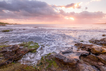 Fototapeta premium Dramatic Coastal Sunset or Sunrise Over Punta Prima, Menorca. Vibrant Sky, Rocky Shoreline, Gentle Waves, Peaceful Seascape, Mediterranean Dawn