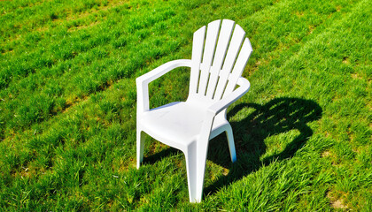 White plastic chair on green lawn in bright sunlight  