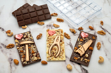 Novel artisanal white and dark chocolate bars with golden chocolates in the shape of tools and nuts glued on, ideal for gifts.