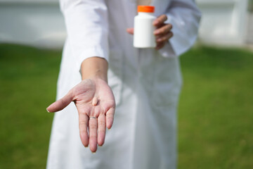 Doctor with stethoscope who is standing in Hospital garden  is holding an medicine bottle to assess...
