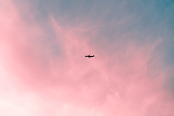 Passenger plane flying high in beautiful pink and blue pastel sunset or sunrise sky with wispy cirrus clouds, creating a dreamy and romantic travel concept