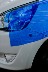 Car with protective blue film on headlight at repair shop before bodywork