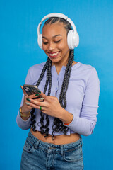 Young woman enjoying music and browsing smartphone on blue background