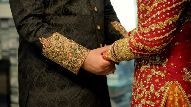 Wedding couple hands while holding each other, dressed in traditional red and black Asian clothes, Elements of hindu wedding. Close up