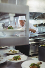 Male chef leaning over counter arranging garnishes on porcelain plates on pass rack in kitchen