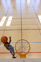 African American man in blue jersey leaping and dunking orange basketball into hoop on gym floor © WavebreakMediaMicro