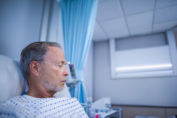 Obraz premium Senior man reclining on hospital bed, resting on pillow beside IV pump and monitor, copy space