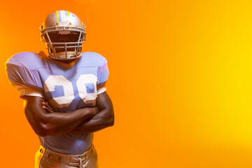 Football player standing in studio against orange backdrop, wearing number 99 jersey and helmet