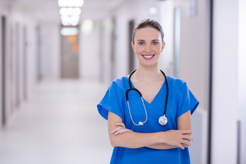 Female healthcare worker standing in hospital corridor wearing blue scrubs and holding stethoscope