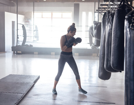 Fototapeta Boxer practicing punches on heavy bags in industrial boxing gym, showing ring and foam mats behind