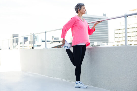 Woman performing standing quadriceps stretch on rooftop terrace overlooking city skyline