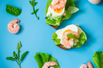 Appetizing breakfast with shrimp, egg and greens on top on blue background