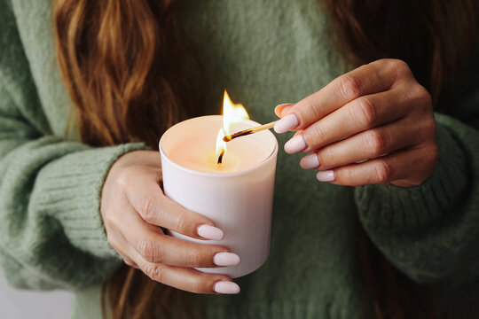Lighting a scented candle. Warm relaxing atmosphere. Woman holding a match. Cozy home ritual. Aromatherapy and calm lifestyle. Peaceful mood with fire. Natural self-care evening moment.