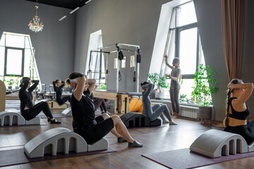 Group of women doing exercises on back spine corrector. Reformer pilates studio machine for fitness workouts in gym. Fit, healthy and strong authentical body. Fitness concept.