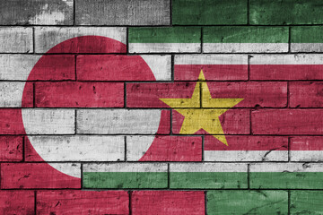 colourful painted big national flag of suriname and flag of greenland on a massive old brick wall background. concept