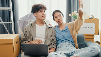 Young happy Asia couple sit on sofa couch use computer laptop online shopping furniture from decoration store in living room at home. Husband wife move new house, Apartment Rent And Ownership Concept.