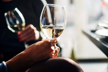 Hand holding white wine glass with golden light bokeh background. Elegant wine tasting restaurant...