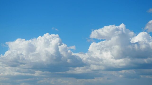 A breathtaking display of fluffy white clouds billows and shifts gently against the vibrant blue sky. The peaceful atmosphere invites contemplation and appreciation for natures beauty