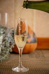 Champagne pouring into flute glass with autumn pumpkin decor. Fall celebration with sparkling wine...