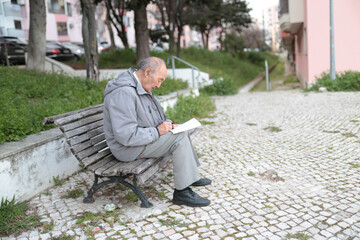 Fototapeta premium Senior man writing on paper while sitting on bench outdoors