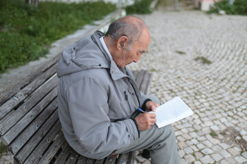 Obraz premium Elderly man writing on notebook while sitting on bench