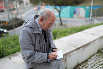 Elderly journalist writing notes outdoors wearing earphones