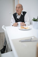Senior man enjoying breakfast with wireless headphones at home