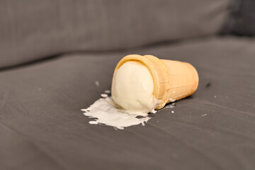 Vanilla ice cream cone lies on grey fabric, melting gradually. Soft lighting creates casual and...