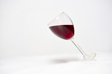 Wine glass tilted on clean white surface. Deep red liquid creates contrast. Minimalistic composition emphasizes elegance, balance, and simplicity