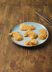 Prepared for deep frying raw chicken nuggets coated with flour, egg and breadcrumbs on ceramic plate on brown wooden background. Recipes chicken.