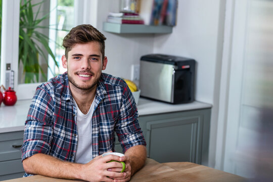 Man sitting at kitchen table holding ceramic mug near toaster and fruit bowl gazing at window