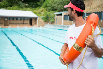 Rescue buoy resting on deck beside lane-marked outdoor pool near pool house with green hillside