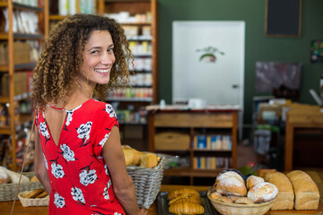 Smiling adult woman standing behind bakery counter displaying wicker baskets of loaves, copy space