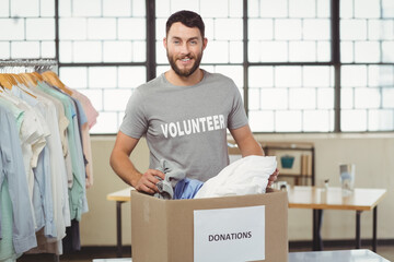 Mid adult man sorting donated clothes at donation box beside clothing rack at community center