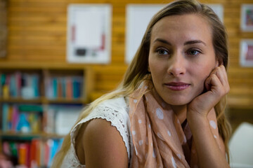 Female supporting chin gazing at library wood panel table featuring shelves and scarf, copy space