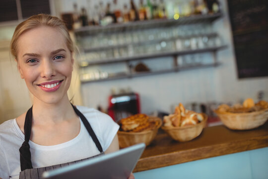 Smiling woman holding tablet behind counter in cafe arranging baskets of pastries by coffee machine - Powered by Adobe
