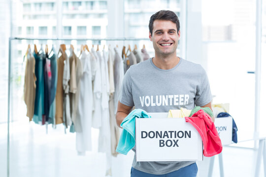 Male volunteer holding donation box filled with colorful clothes at donation center, copy space
