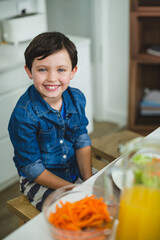 Boy smiling and sitting at dining table at home with bowl of carrots, pitcher orange juice © wavebreak3