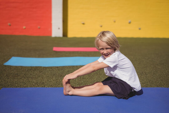 Fototapeta Boy stretching on blue mat on green turf with extra mats near red and yellow wall