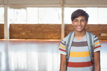 Teenage boy standing on right side in school gym carrying gray backpack, copy space © wavebreak3