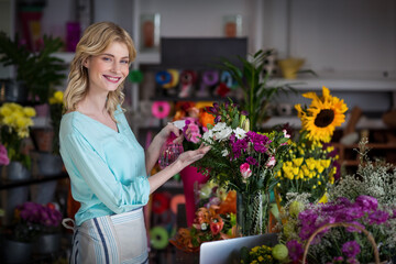 Misting colorful bouquet with spray bottle in clear glass vase on busy shop table with ribbons