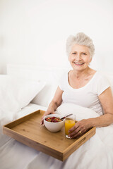 Senior woman sitting in bedroom holding wooden breakfast tray with fruit bowl and orange juice © WavebreakMediaMicro