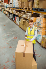 Mid adult female warehouse worker sealing cardboard box with tape dispenser in aisle, copy space