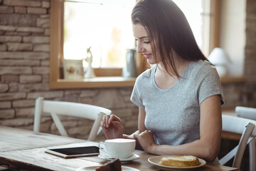 Woman sitting at table in cozy cafe using tablet with coffee, pastry and cake, copy space