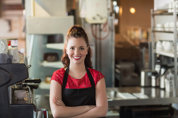 Teenage barista smiling behind cafe counter wearing red top and black apron with espresso machine