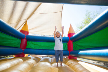Boy bouncing inside brightly colored inflatable bounce castle under beige shade canopy in backyard