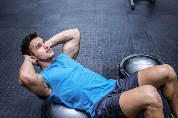 Man performing abdominal crunches on half-sphere BOSU trainer at gym with weight machines