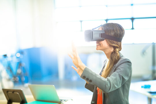 Virtual reality headset projecting immersive scenario on desk with laptop in office, bicycle behind - Powered by Adobe